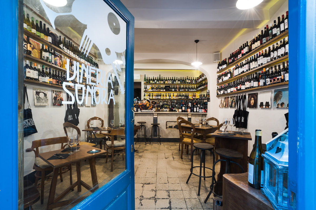 Blue windowed door opening up into a wine bar in Florence with several tables and shelves of bottles lining the walls