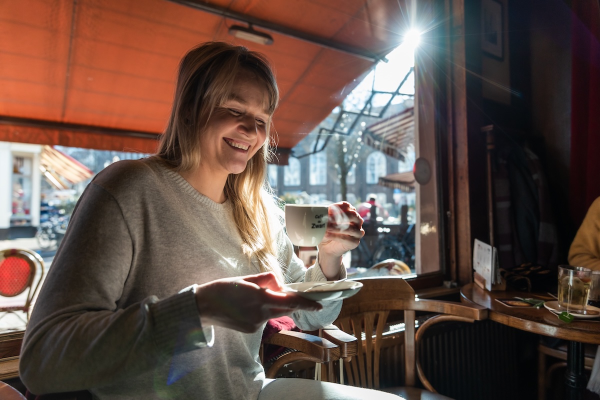 A woman smiling and drinking a hot beverage in a cafe.