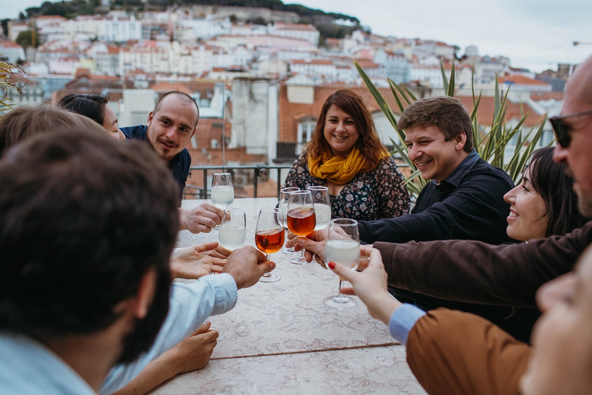 Group of people sitting outside in Lisbon raising a small glass of bright orange wine or port