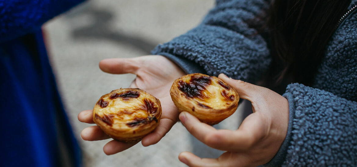 A person holding custard tarts in Lisbon, explaining Portuguese food facts