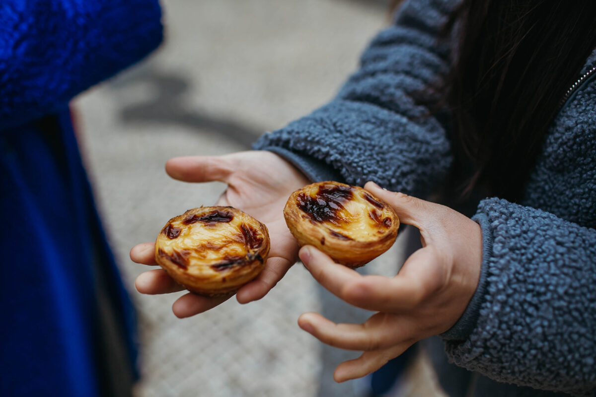 A person holding custard tarts in Lisbon, explaining Portuguese food facts