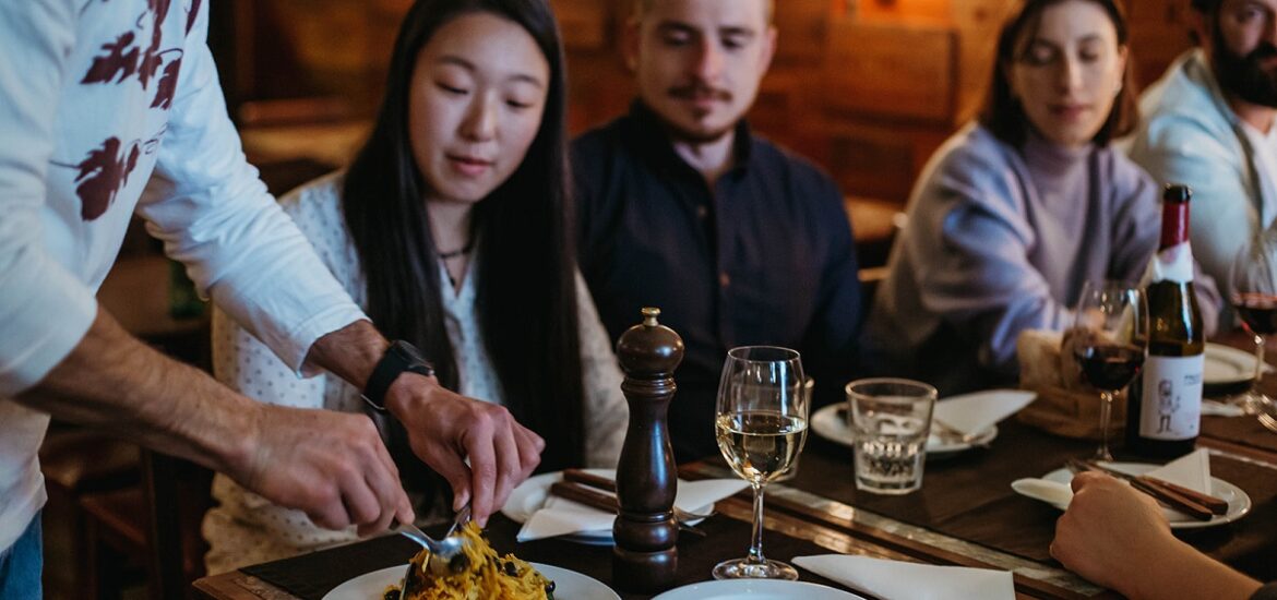 Chef cutting dish of bacalhau a bras at a restaurant table in front of a group of diners