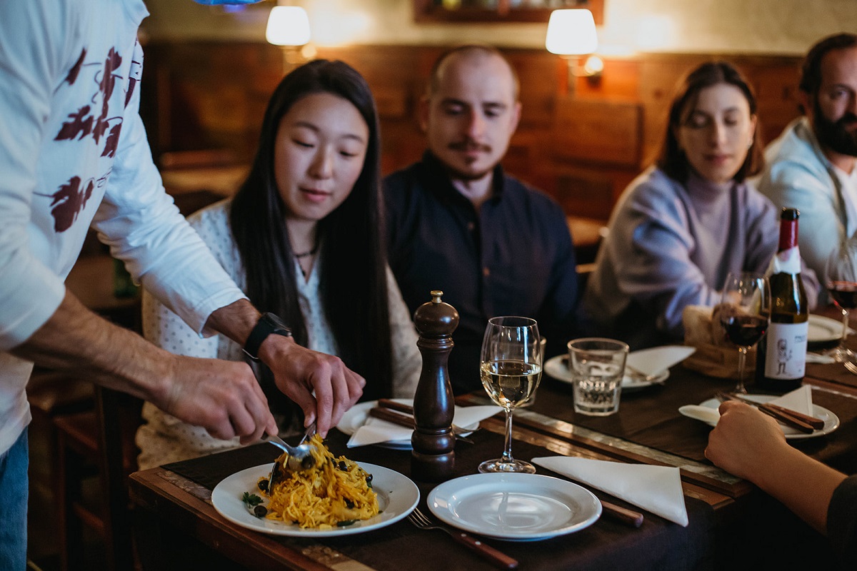 Chef cutting dish of bacalhau a bras at a restaurant table in front of a group of diners