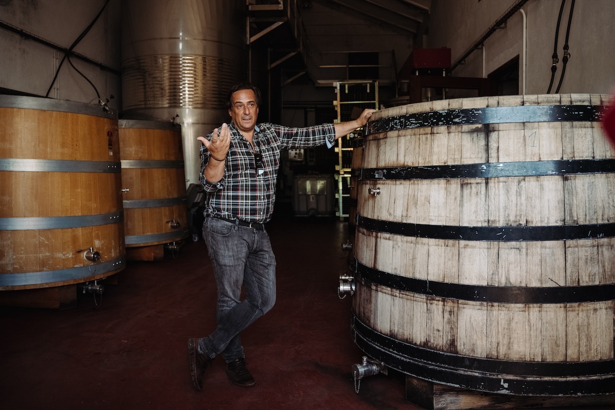 Winemaker standing next to a wine barrel explaining the wine making process.
