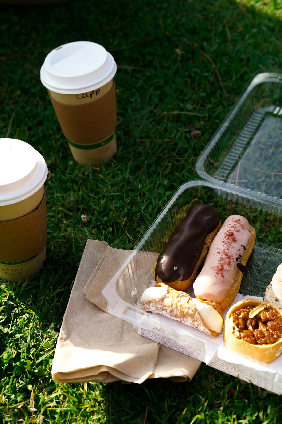 An assortment of french pastries in a container and two coffees. 