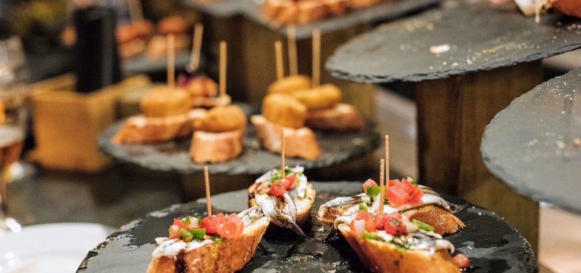 Small slices of bread topped with anchovies and diced vegetables on a black plate.