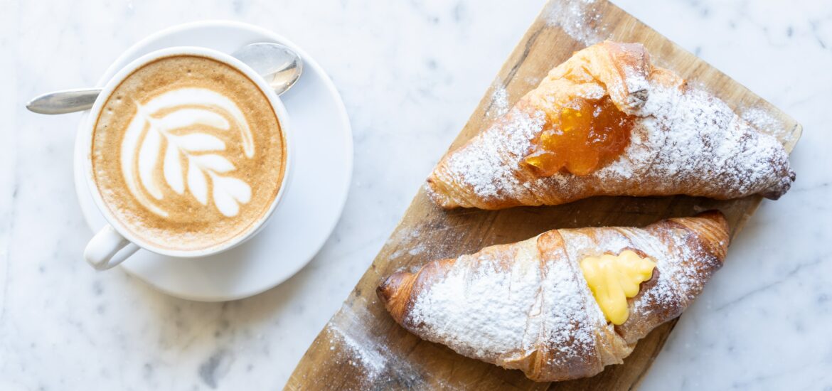 Wooden plate with two Italian cornetti pastries and a cappucino