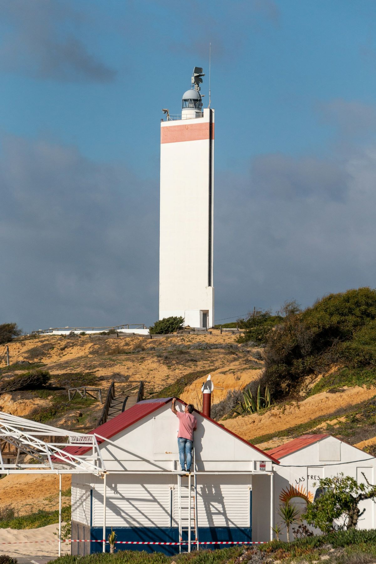 A person working on a house with a lighthouse in the background at Matalascañas. 