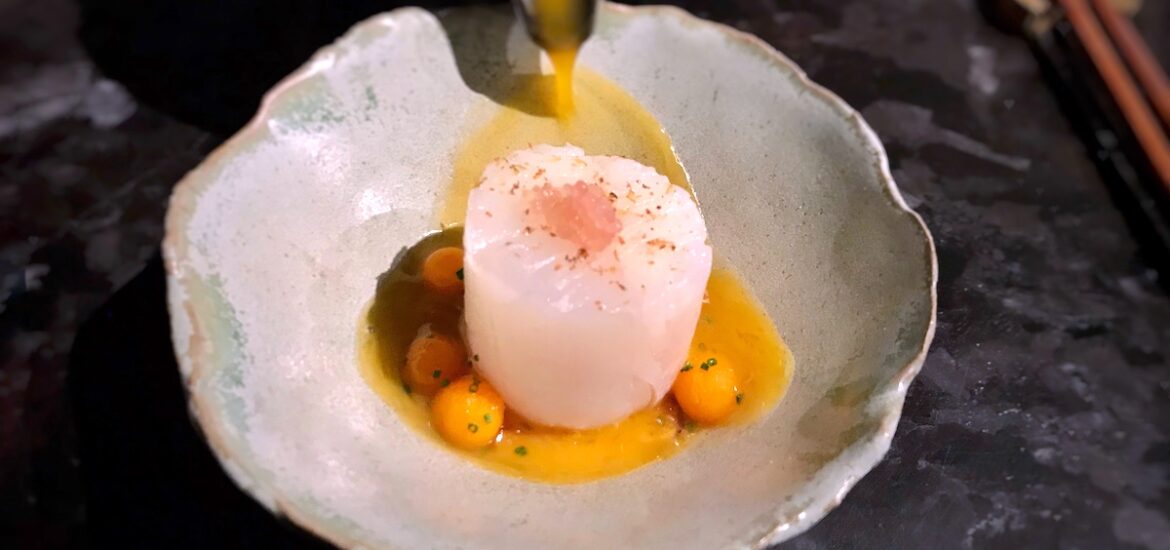 Brown sauce being poured over modernly presented halibut dish