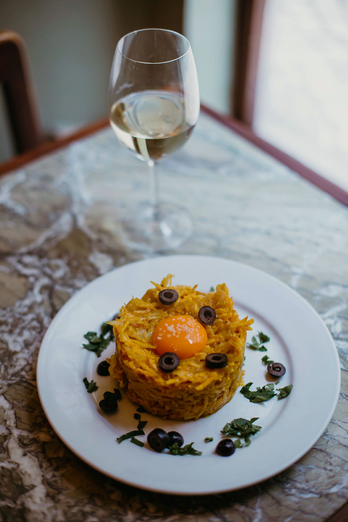 Bacalhau à Brás on a ceramic plate next to a glass of white wine. 