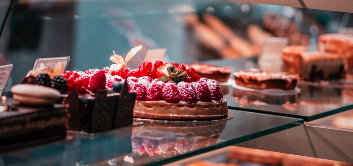 Small cakes garnished with strawberries and other fruits in a bakery display case.