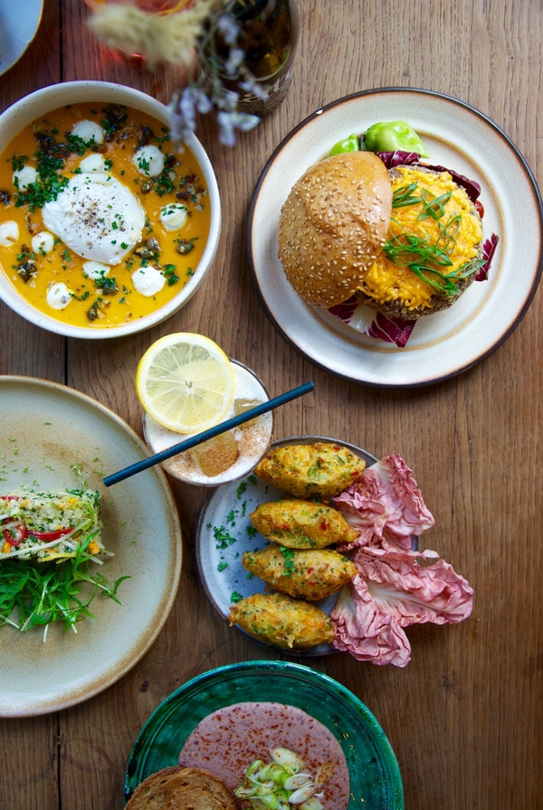 plates of colorful food like burgers and croquettes on a wooden table.