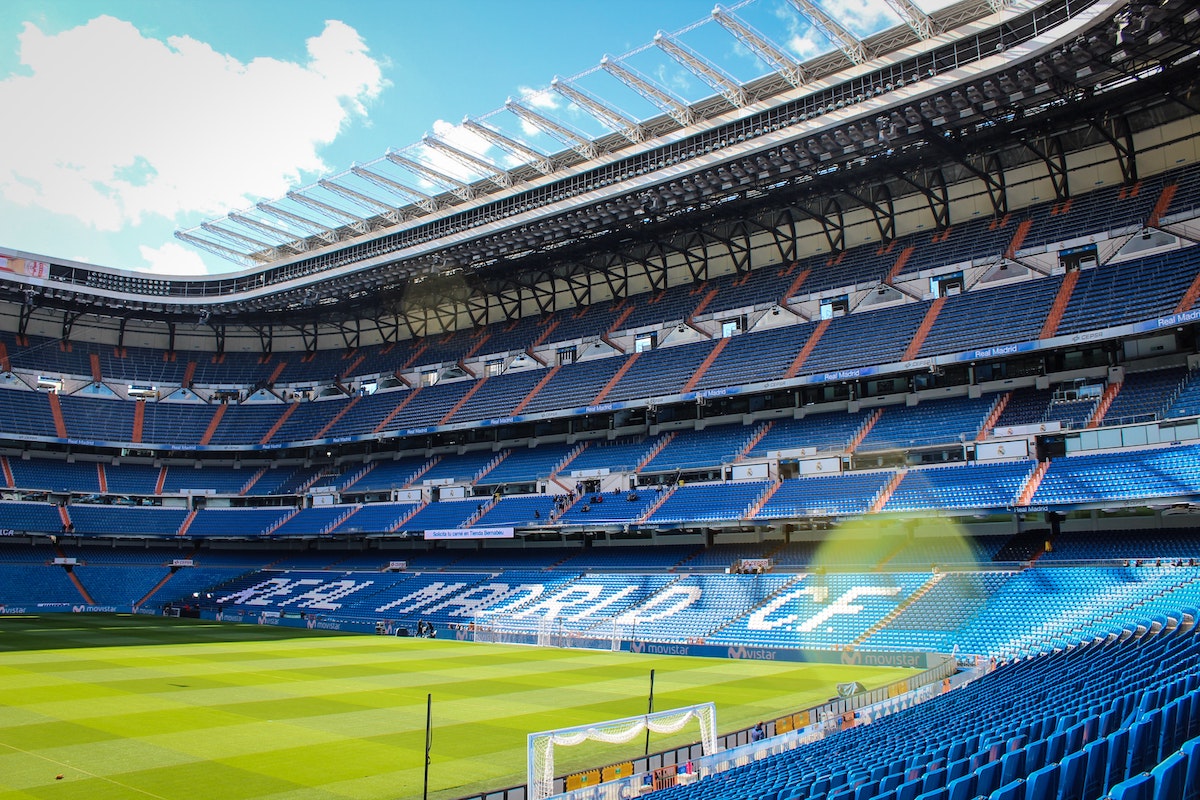 View inside a large empty soccer stadium with green turf and blue seats, some of which are painted white to spell out REAL MADRID CF.