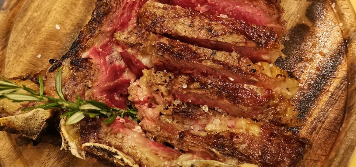 Overhead shot of sliced rare steak on a wooden plate garnished with herbs