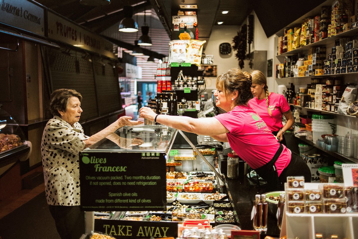 An elderly woman purchasing olives at an indoor market stall