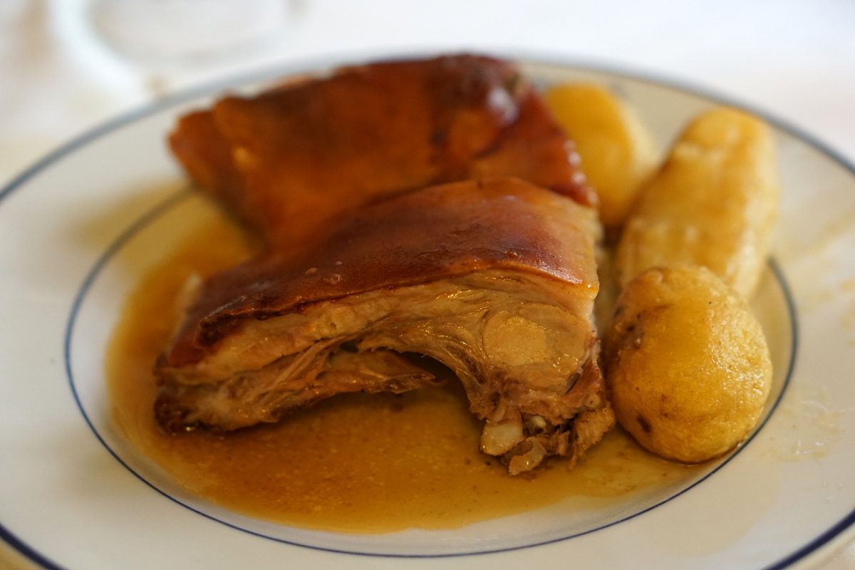 Piece of roast pork in its sauce on a plate beside roast potatoes