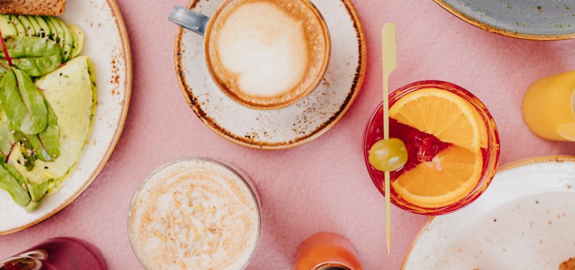 Overhead shot of brunch items on a table including toast, omelets, cocktails and coffee