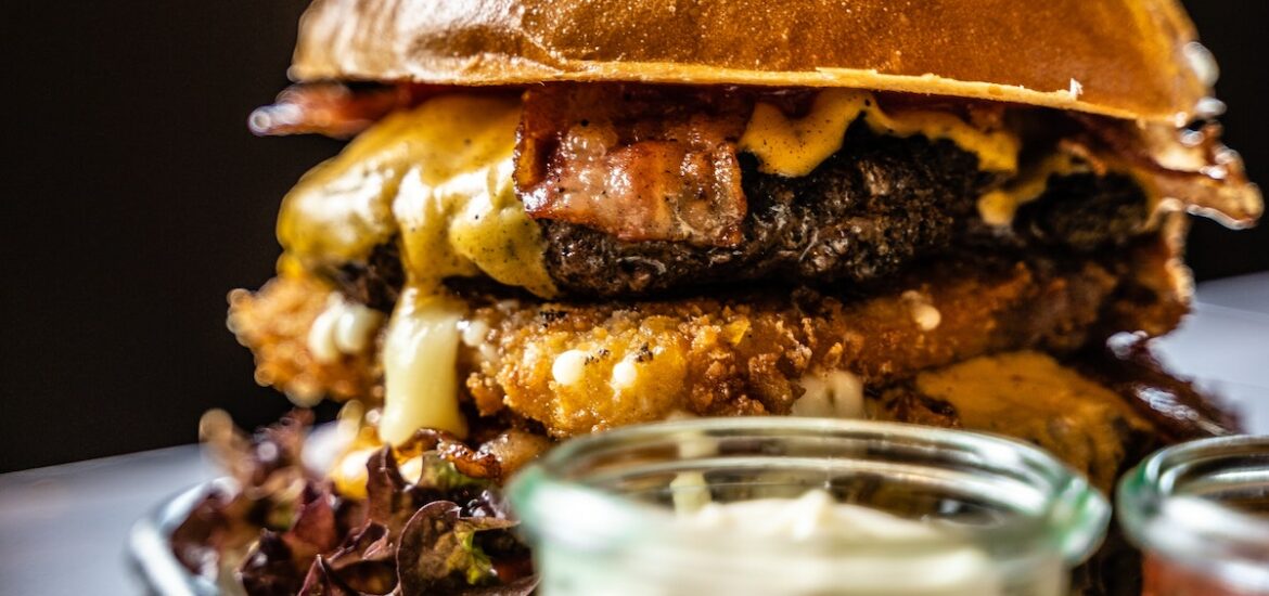 Cheeseburger on a tray with a small container of white sauce in front of it.