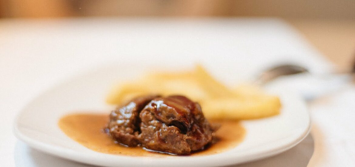 Meat in sauce and french fries on a white plate.