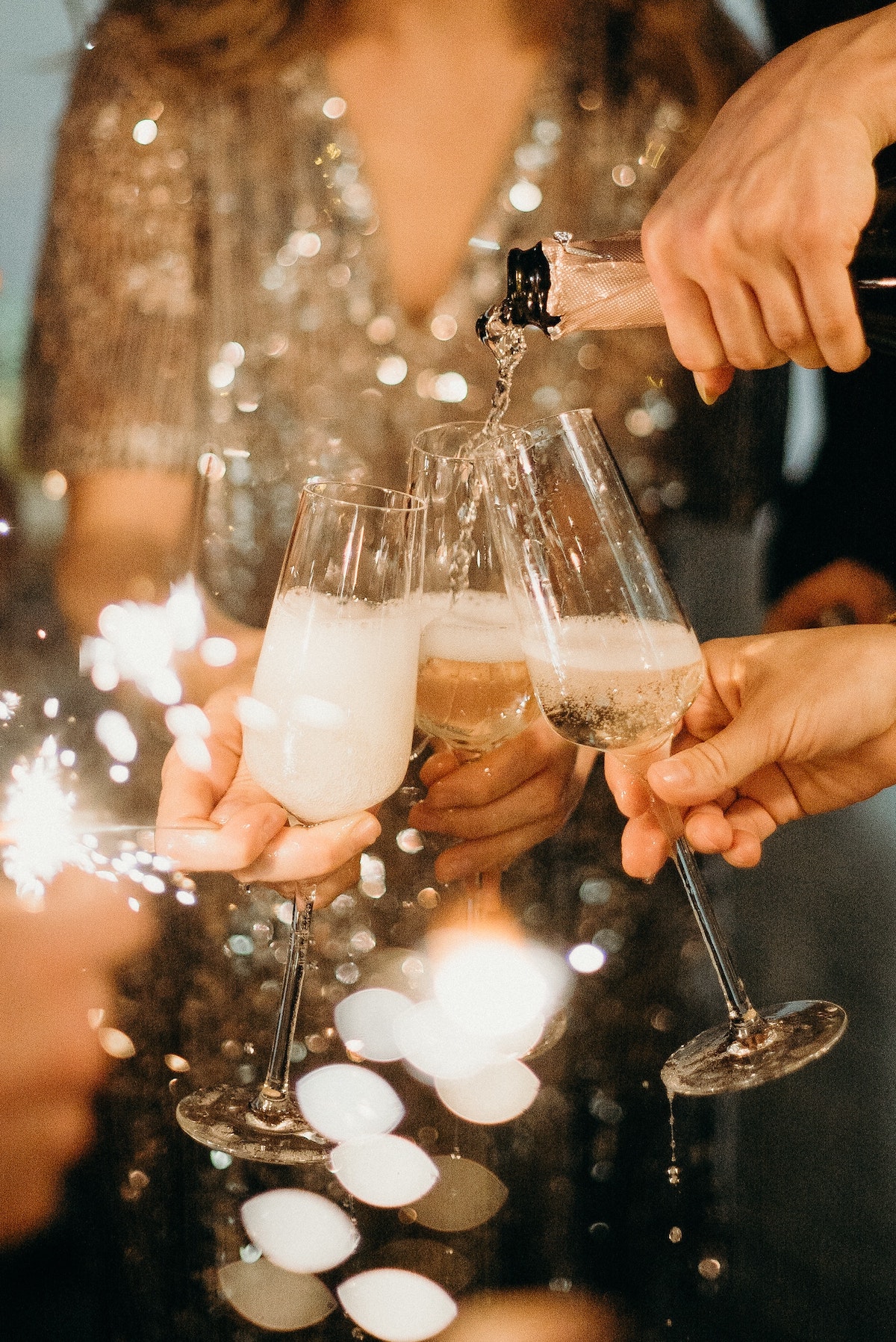 Champagne being poured from a bottle into three flutes held in people's hands.