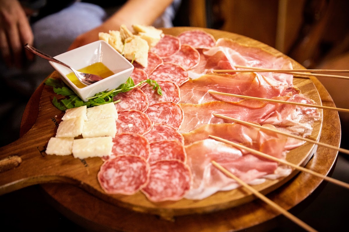 Close up of an Italian charcuterie board with slices of prosciutto, salami, various cheeses, and a small dish of honey. A perfect option for lunch in Madrid. 