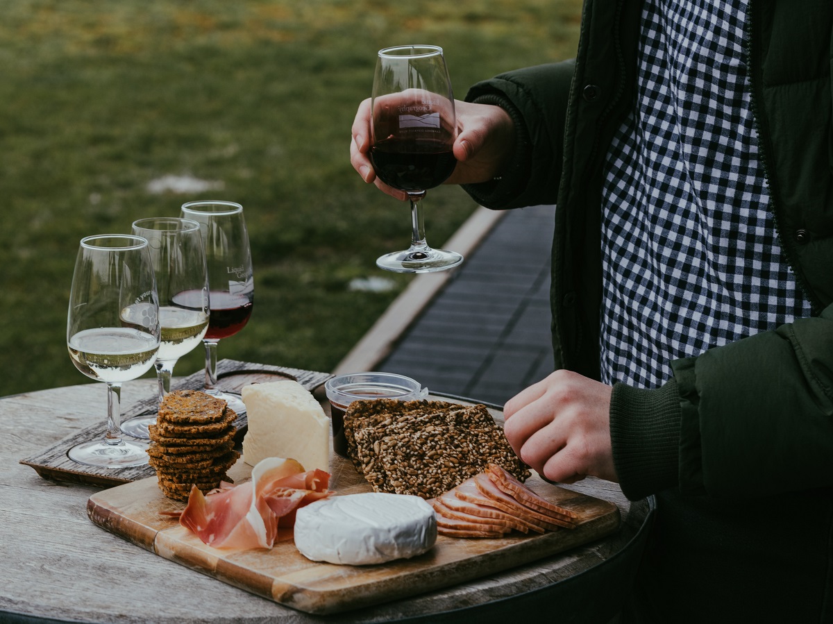 Person enjoys a charcuterie board with cheese jam and glasses of wine outside