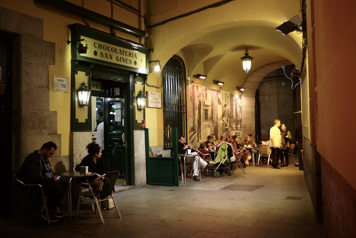 Exterior of a cafe in an arched passageway with people sitting at the terrace tables.