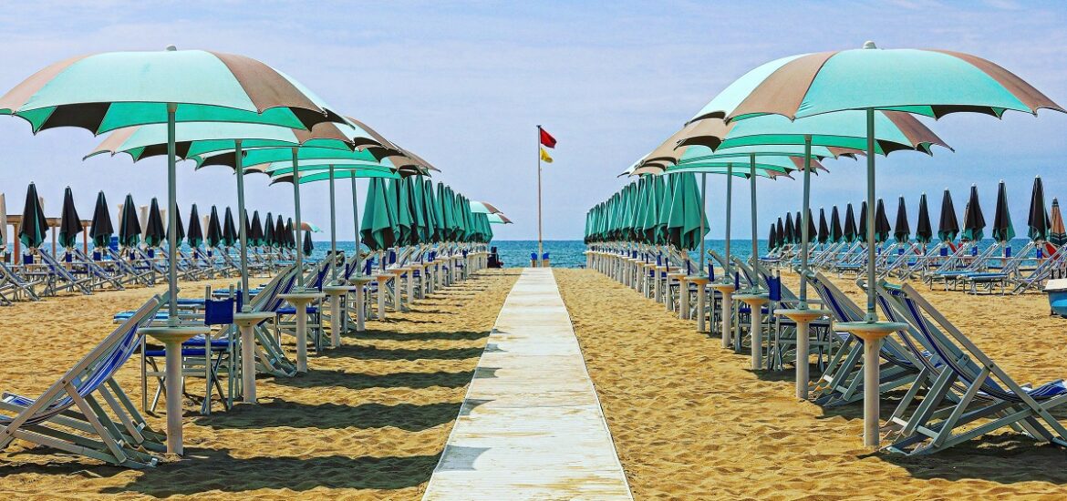 Sandy beach filled with beach chairs with umbrella and a pathway leading to the water