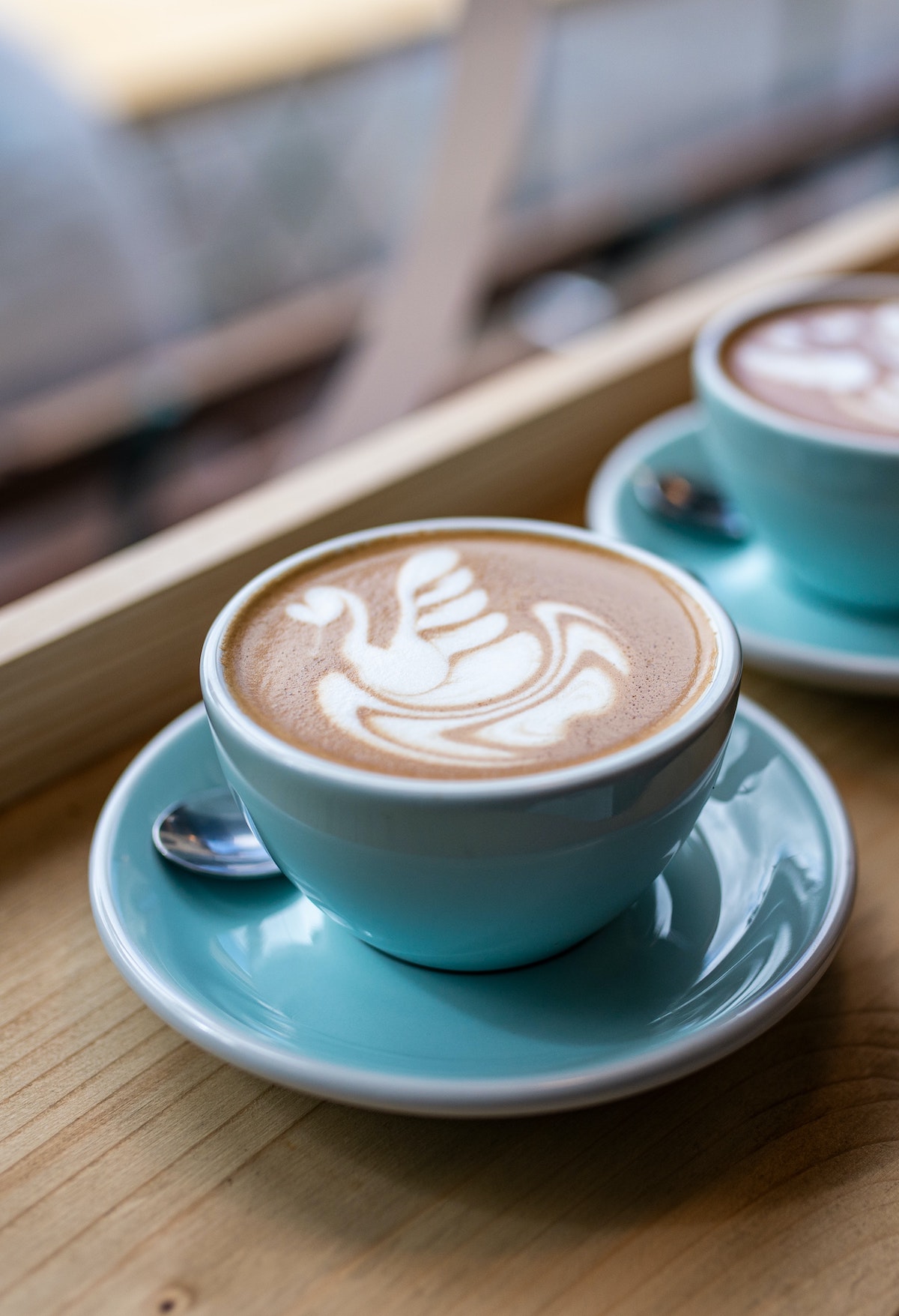 Latte with milk drawn in the shape of a swan served in a teal cup.