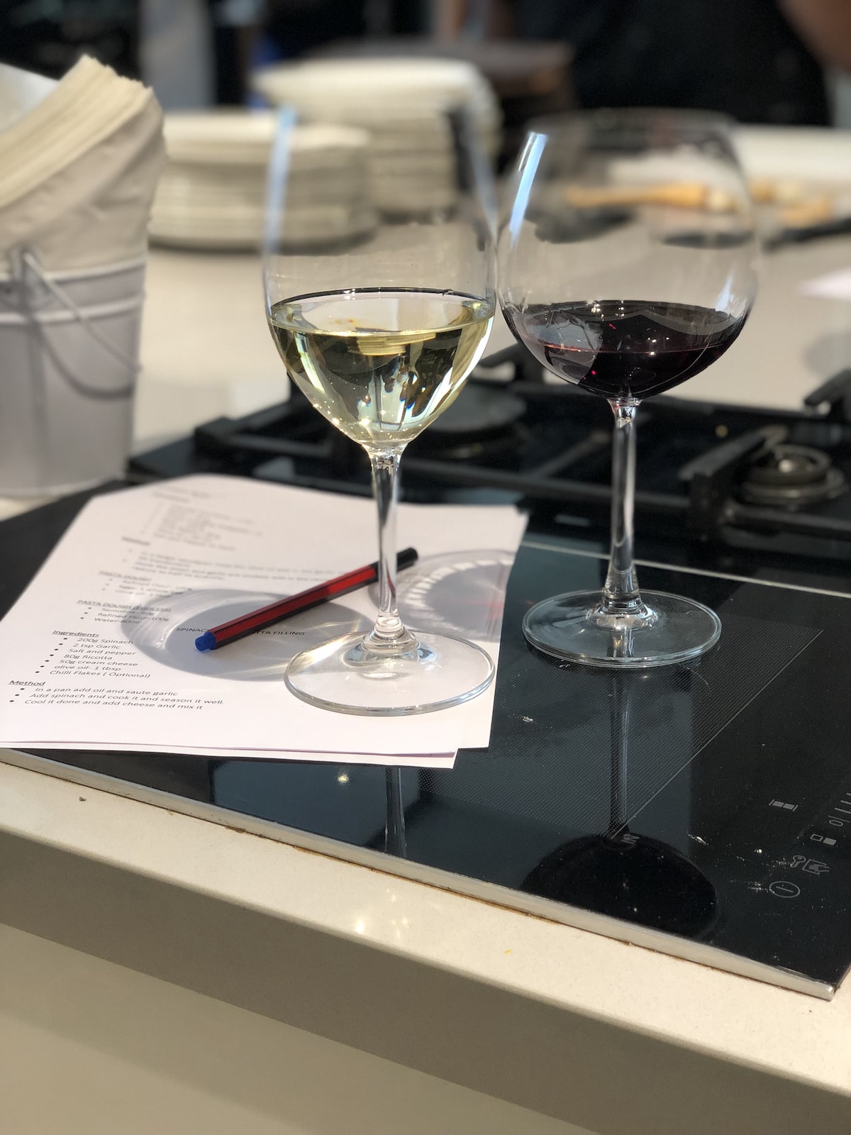 Two glasses of red and white wine beside a pen and sheet of paper on a kitchen surface