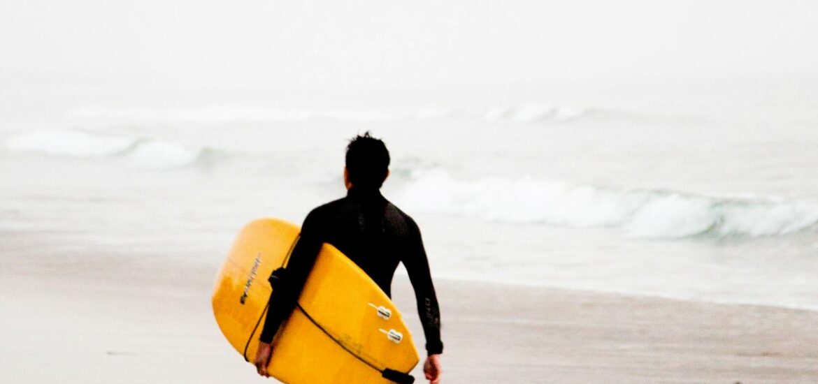 person with surfboard walking into ocean at a beach surfing in San Sebastian