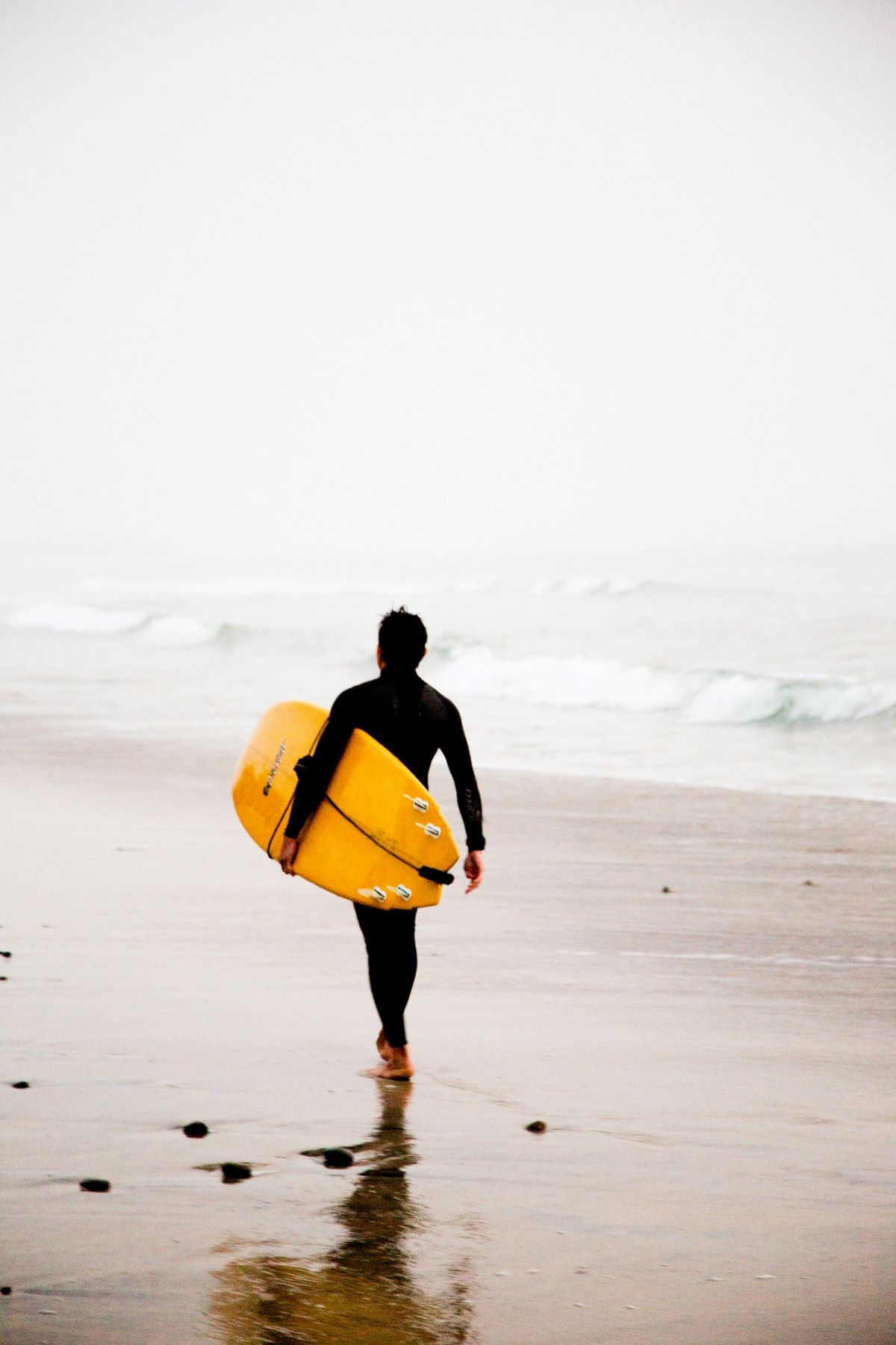 person with surfboard walking into ocean at a beach surfing in San Sebastian