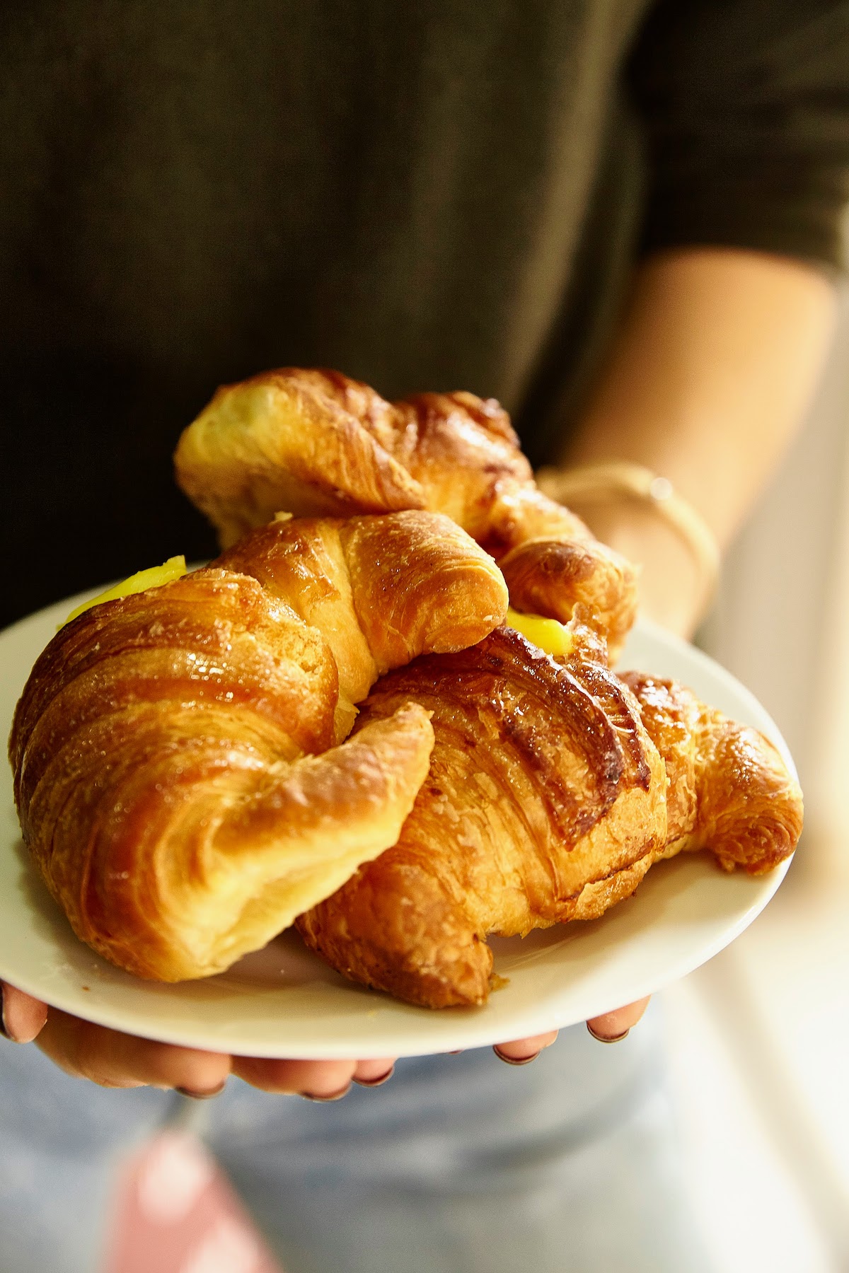 Three Italian-style croissants on a white plate in a person's hand