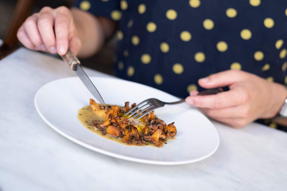 Close up of a person's hands cutting food on a white plate