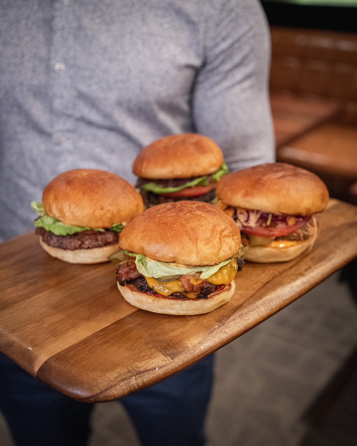 Man holding a wooden board with 4 hamburgers