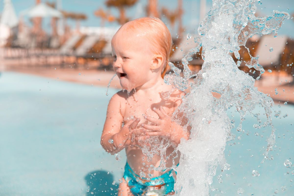 Child standing at a water park playing in a fountain. 