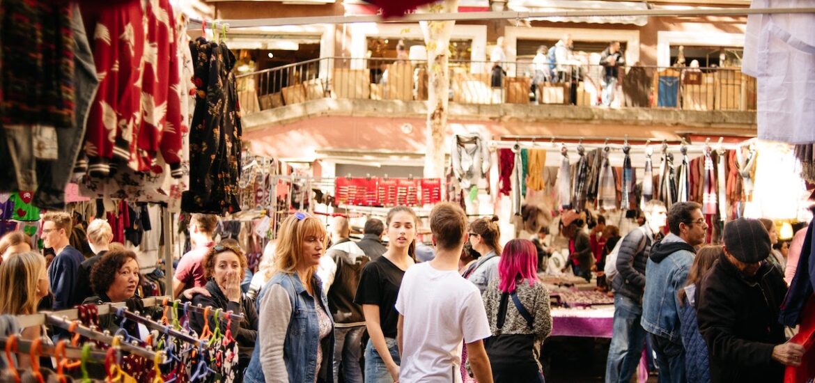 Crowd of people walking by clothing stalls at a flea market.