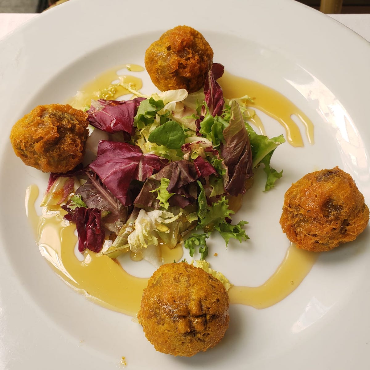 Four fried croquettes and a leafy green salad on a white plate drizzled with honey