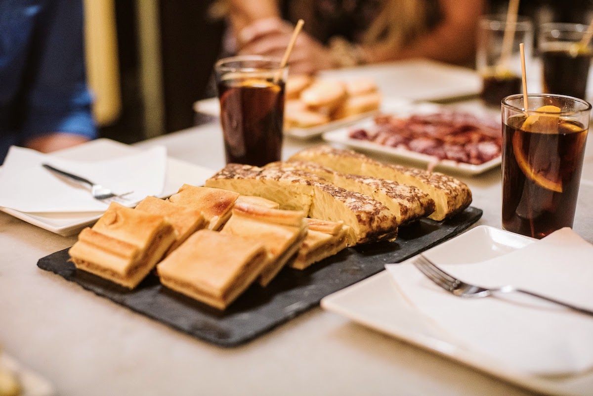 Slices of Galician empanada and Spanish potato omelet on a black tray