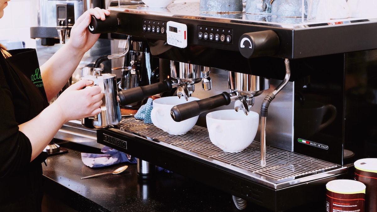 Barista making two cups of coffee at an espresso machine.