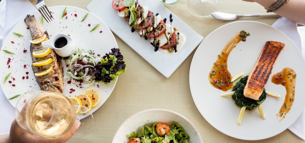 Couple sharing a restaurant meal with many small dishes including salad with shrimp, grilled fish, salmon, and sliced tomatoes