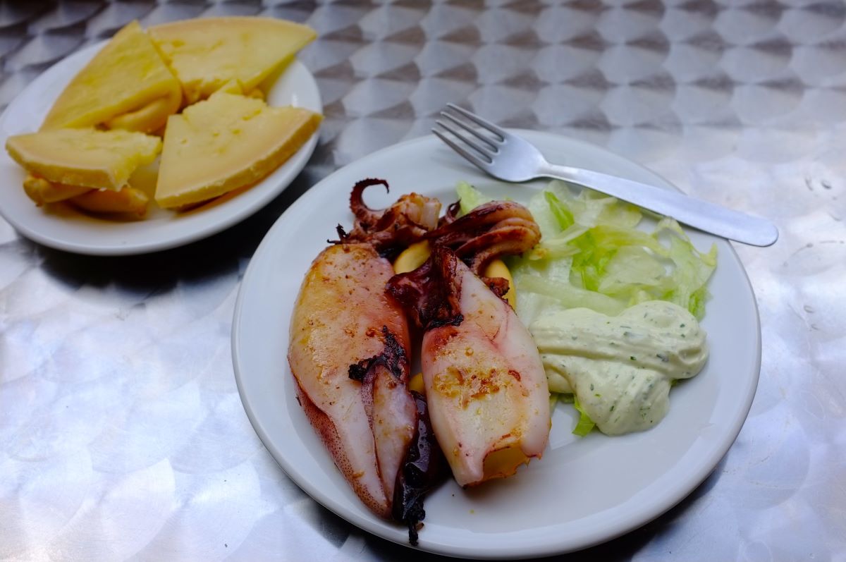 One white plate with slices of cheese and another with squid 