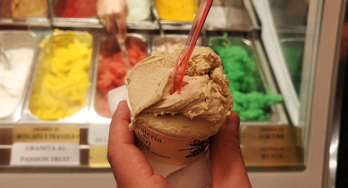 Tiny cup of ice cream in front of multi-colored sorbets at Gelateria dei Neri in Florence.