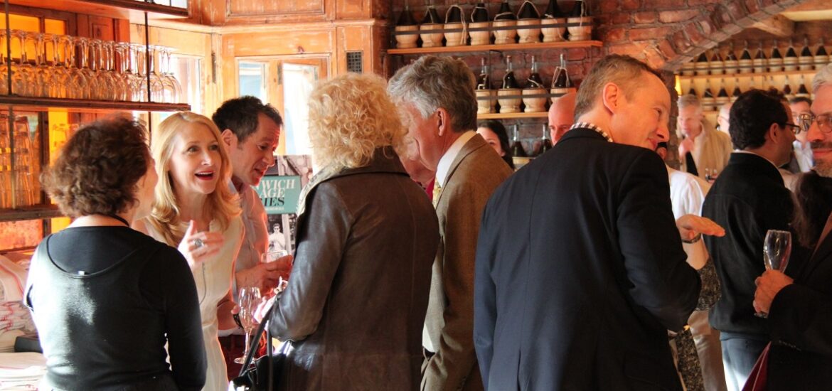 Lively group in a sunlit restaurant chats with glasses of wine in hand