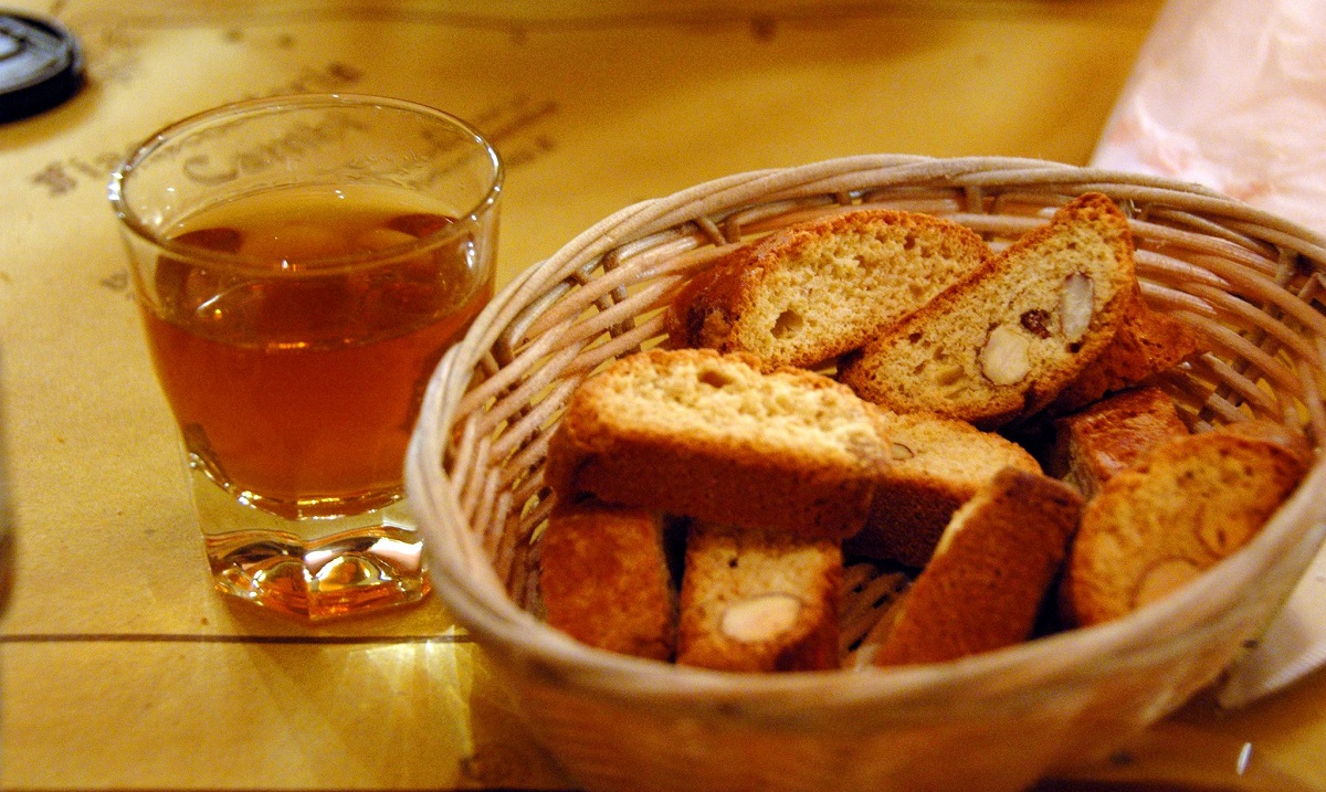 A basket of hard, yellow cookies and a small glass of amber liquid