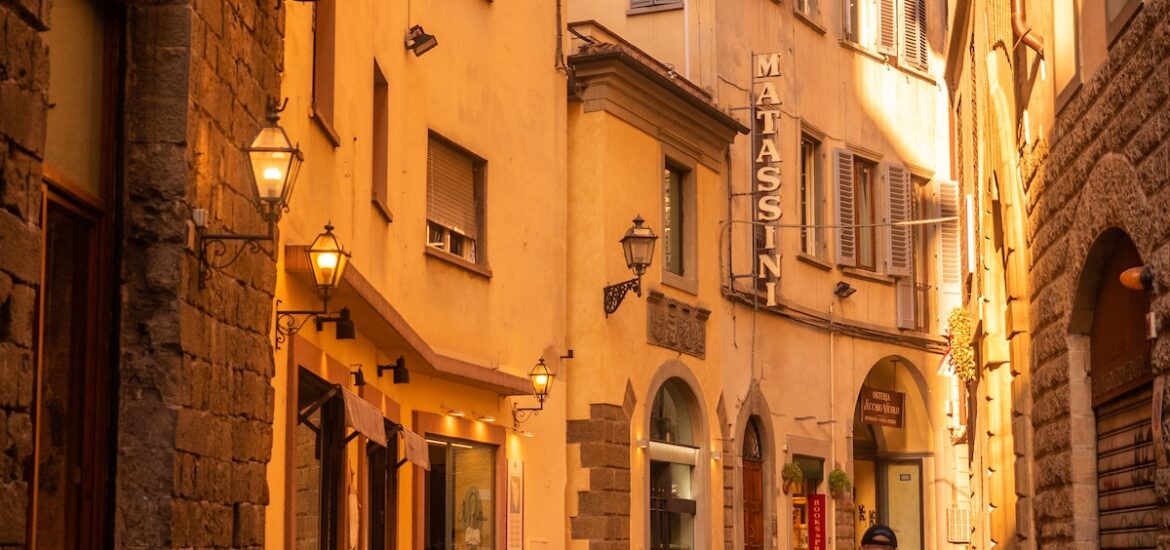 A person in a red jacket riding a bike on a pedestrian street in Florence