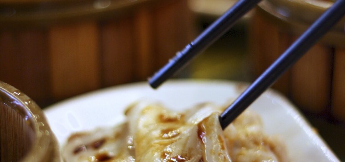 Pair of chopsticks poised above a Chinese dumpling dish in soy sauce