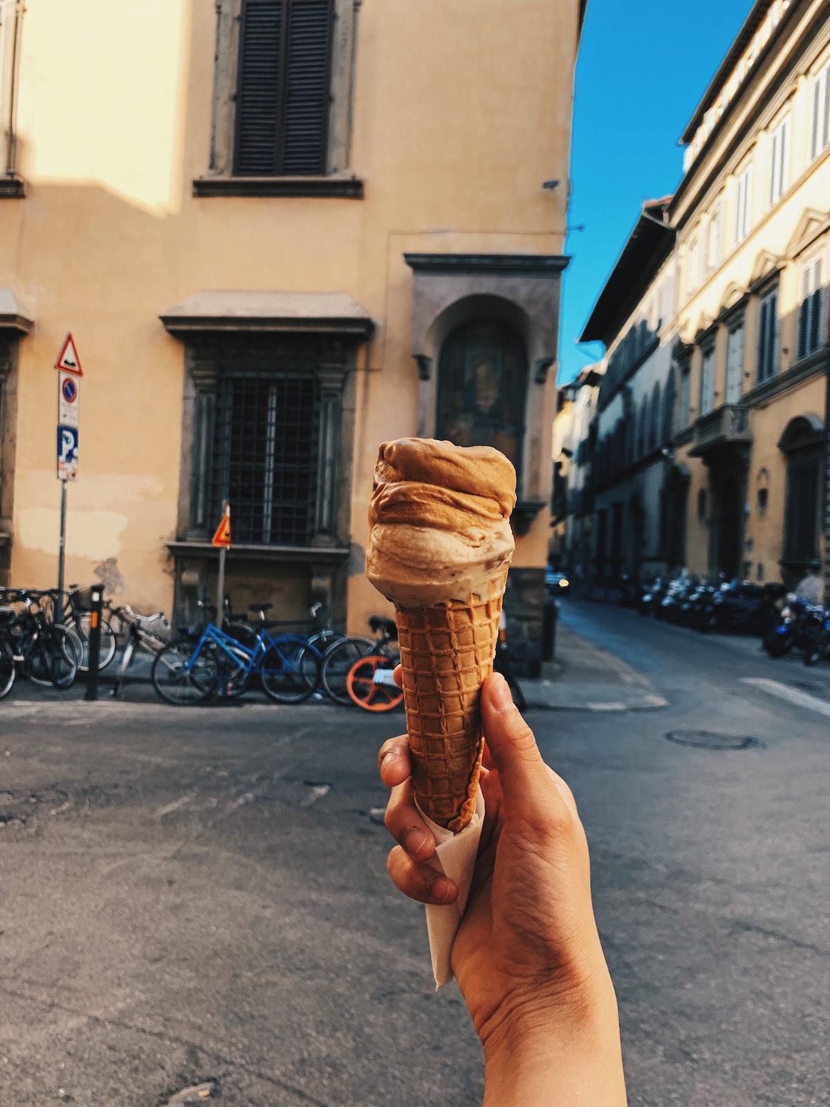 Person's hand holding up a gelato cone in front of a building