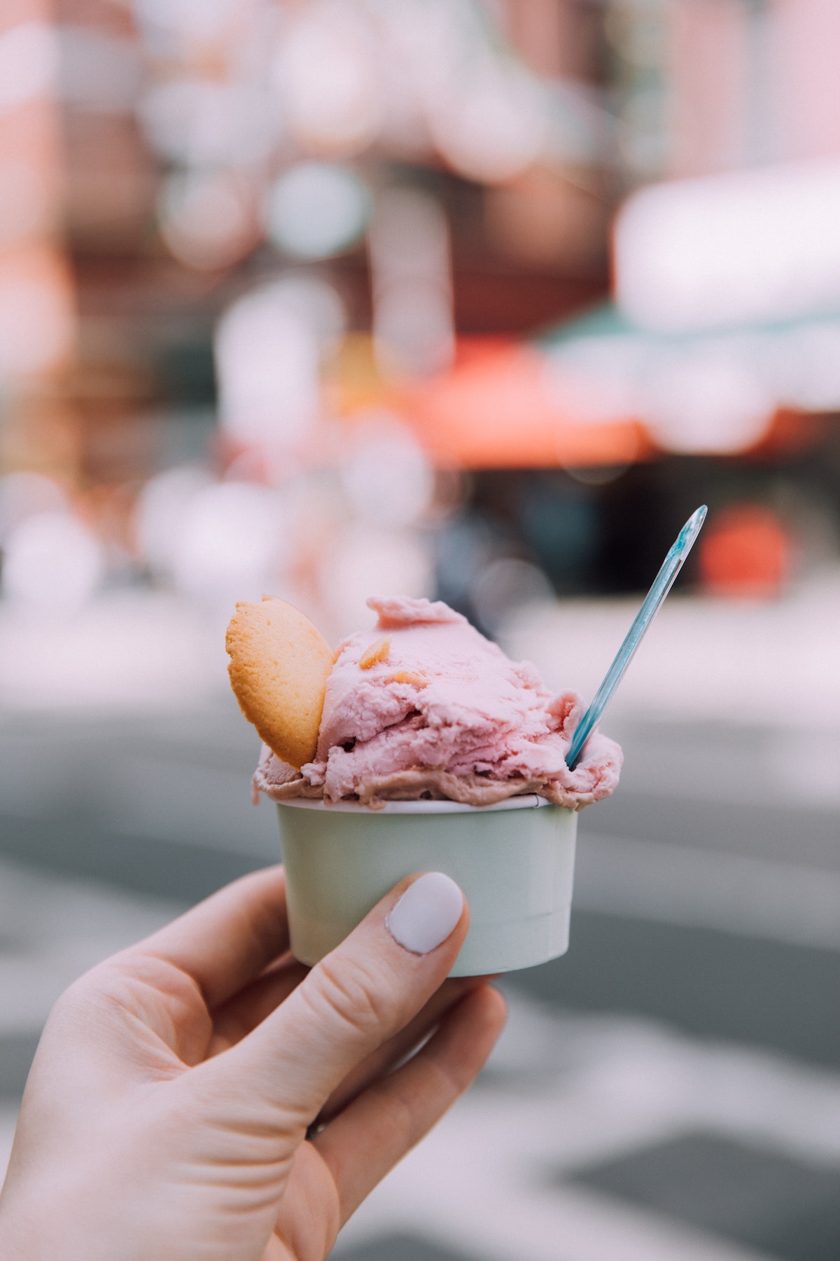 Person's hand holding a small cup of pink gelato garnished with a cookie