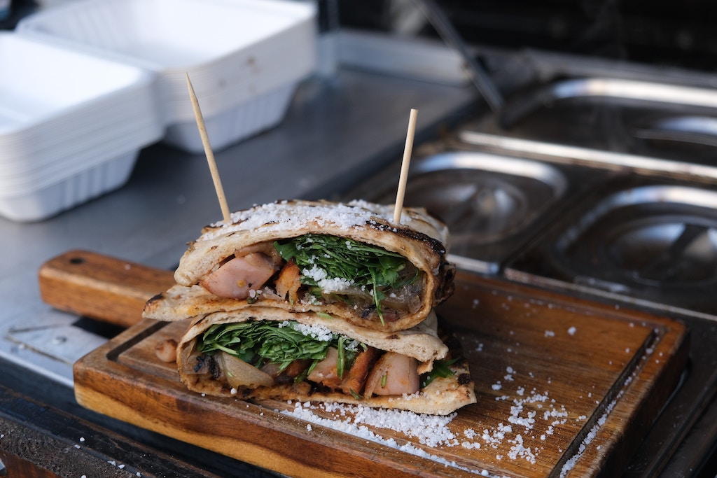 Wooden board sprinkled with thick salt featuring a sandwich with meat and greens